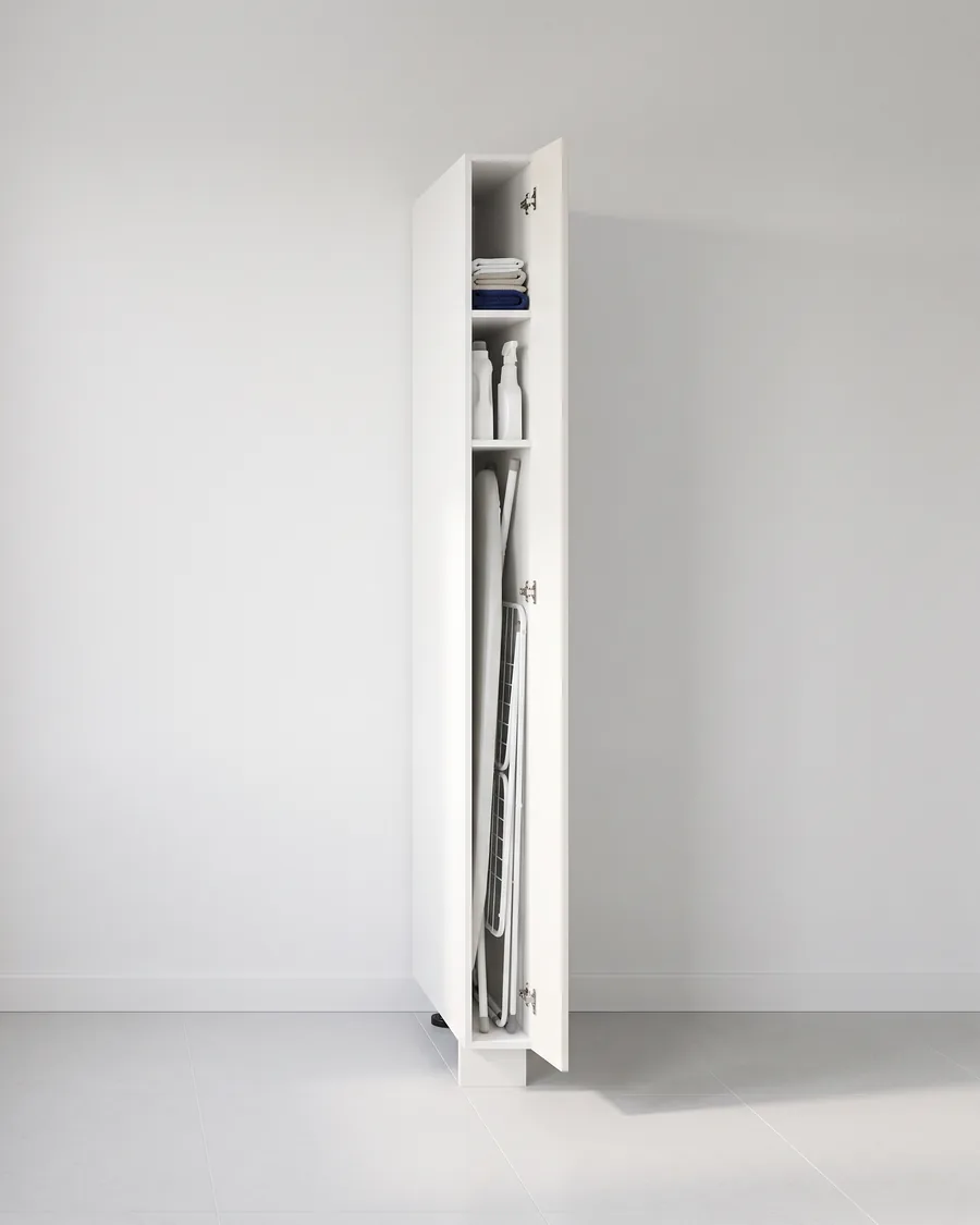 Smalle kast van 15 cm met witte deur open: onderin een opgeklapte strijkplank en een droogrek op hun kant, daarboven twee schappen met flessen en doeken.