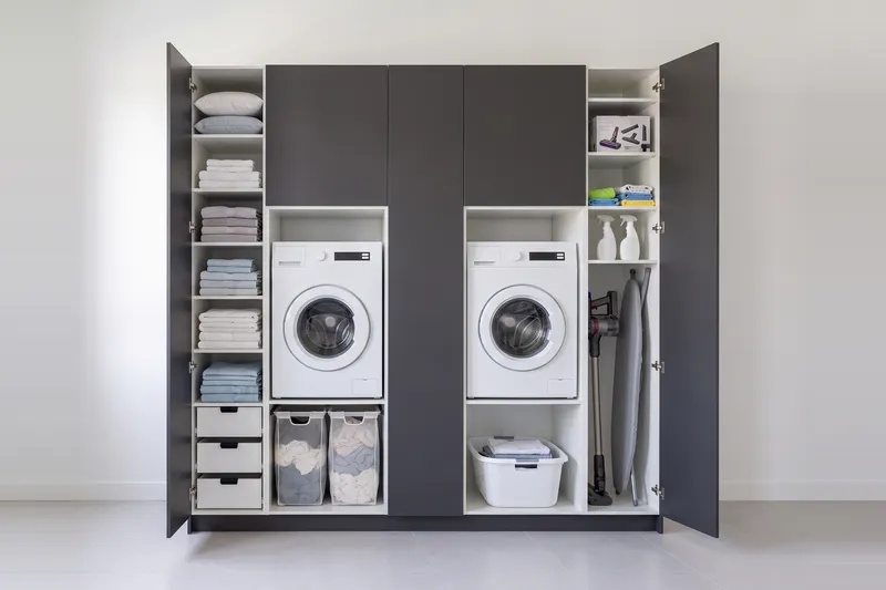 Impressie: twee wasmachinekasten met drie kasten, 254 cm breed en 250 cm hoog, fronten in antraciet, met deuren open.