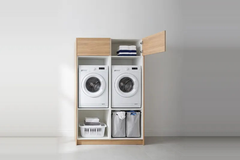 Impressie: twee wasmachinekasten, 133,7 cm breed en 210 cm hoog, fronten in naturel eiken, met deuren open.