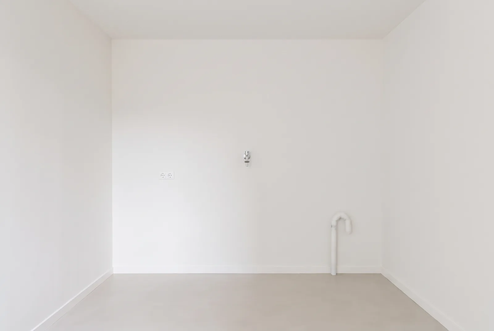 De plek van de kast tegen de muur, met een stopcontact, een kraan en een afvoer.